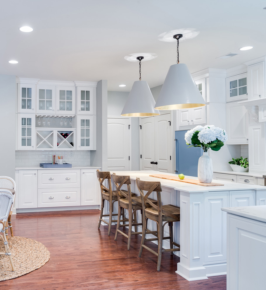 Photo of a traditional l-shaped eat-in kitchen in St Louis with raised-panel cabinets, white cabinets, white splashback, subway tile splashback, coloured appliances, dark hardwood floors, with island, brown floor and white benchtop.