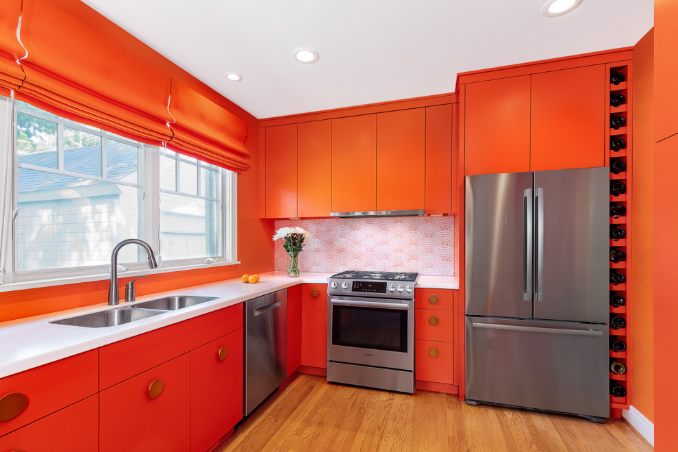 Modern inredning av ett litet vit vitt kök, med en undermonterad diskho, släta luckor, orange skåp, bänkskiva i kvarts, orange stänkskydd, stänkskydd i mosaik, rostfria vitvaror, ljust trägolv, en halv köksö och brunt golv