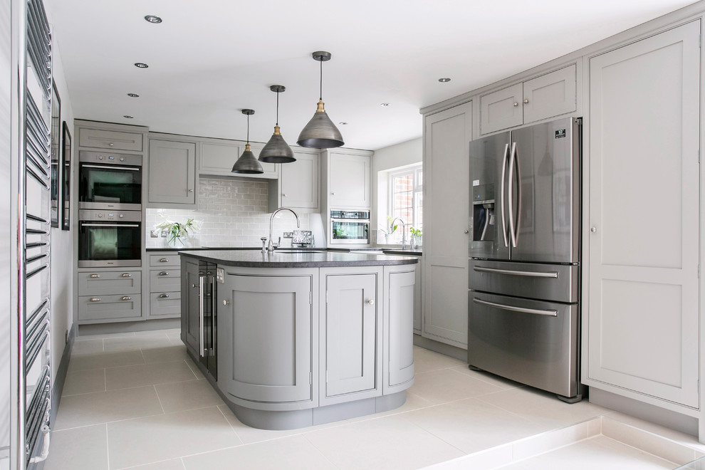 Design ideas for a mid-sized transitional u-shaped eat-in kitchen in Kent with a farmhouse sink, shaker cabinets, grey cabinets, granite benchtops, white splashback, subway tile splashback, panelled appliances, ceramic floors, with island, white floor and black benchtop.