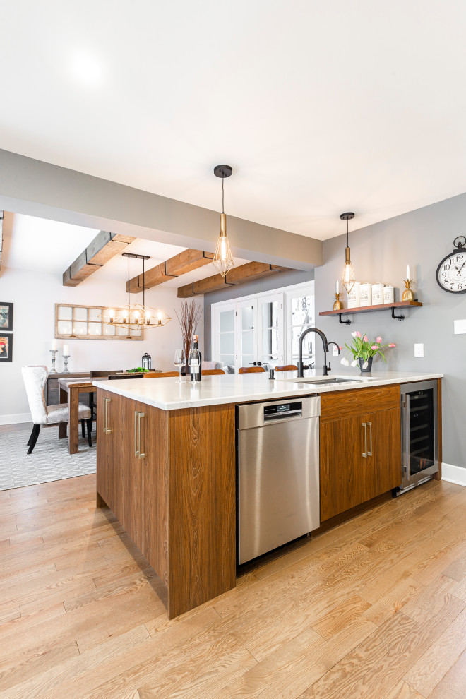 This is an example of a large country u-shaped eat-in kitchen in Montreal with an undermount sink, shaker cabinets, white cabinets, quartz benchtops, grey splashback, mosaic tile splashback, stainless steel appliances, medium hardwood floors, with island, brown floor, white benchtop and exposed beam.