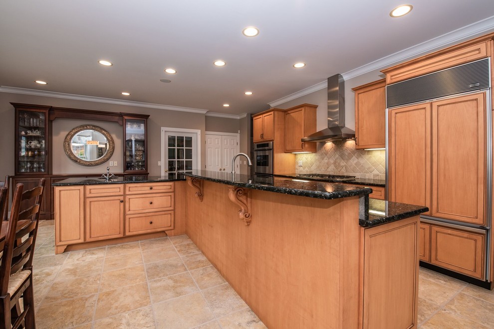 Photo of a large transitional single-wall eat-in kitchen in New York with a drop-in sink, beaded inset cabinets, medium wood cabinets, laminate benchtops, beige splashback, stone tile splashback, stainless steel appliances, limestone floors, with island, beige floor and black benchtop.