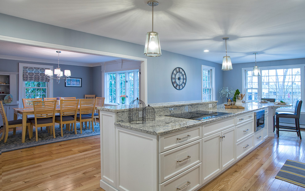 Photo of a large transitional galley eat-in kitchen in Boston with a single-bowl sink, recessed-panel cabinets, white cabinets, granite benchtops, grey splashback, ceramic splashback, stainless steel appliances, light hardwood floors and with island.