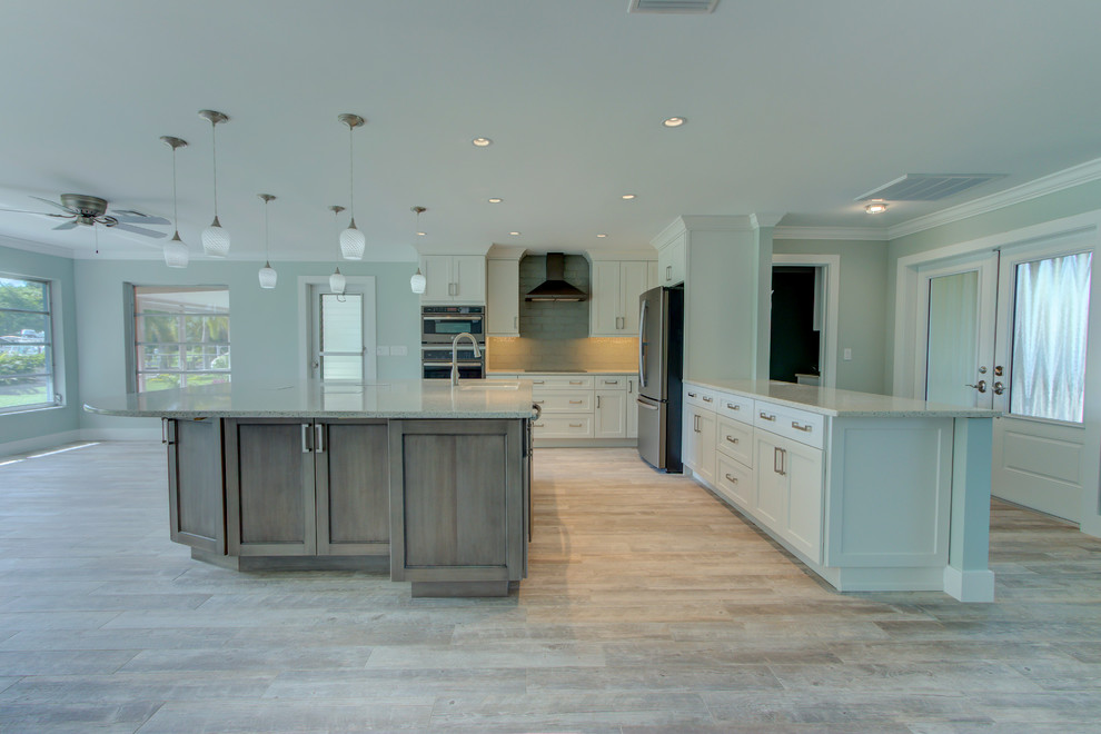 Inspiration for a large transitional l-shaped ceramic tile and gray floor home design remodel with an undermount sink, shaker cabinets, white cabinets, recycled glass countertops, blue backsplash, glass tile backsplash, stainless steel appliances, an island and white countertops