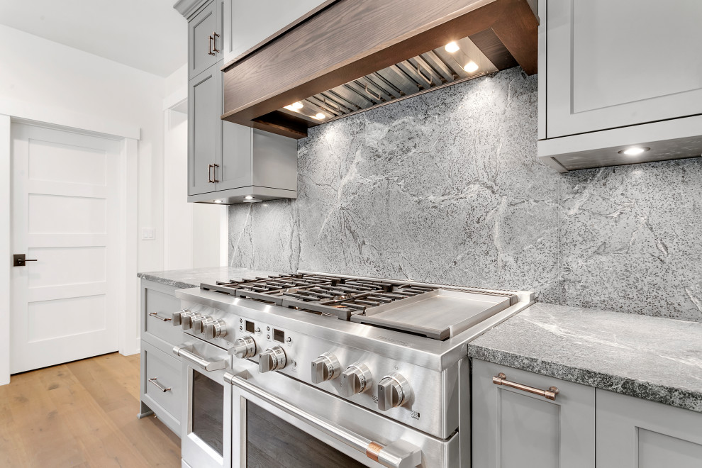 Example of a huge mountain style l-shaped medium tone wood floor, multicolored floor and wood ceiling eat-in kitchen design with an undermount sink, recessed-panel cabinets, gray cabinets, soapstone countertops, gray backsplash, quartz backsplash, stainless steel appliances, an island and gray countertops