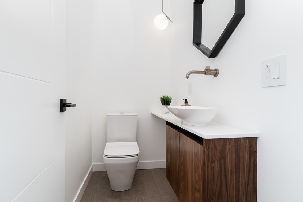 Design ideas for a contemporary powder room in Other with flat-panel cabinets, dark wood cabinets, a one-piece toilet, white walls, dark hardwood floors, a vessel sink, brown floor and white benchtops.
