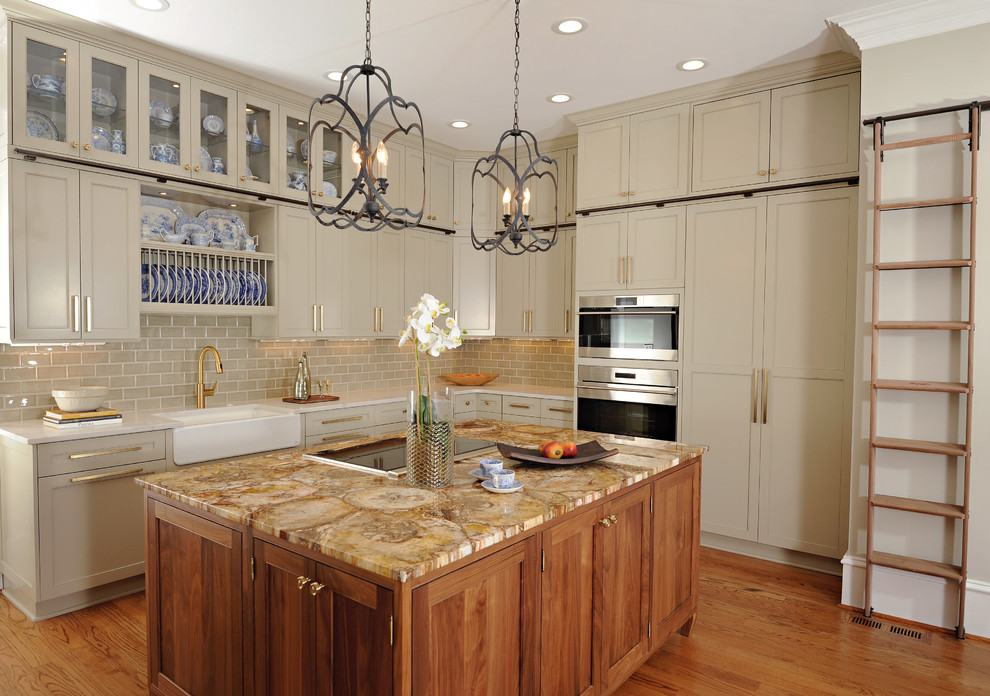 Inspiration for a transitional l-shaped medium tone wood floor kitchen remodel in Atlanta with a farmhouse sink, shaker cabinets, beige cabinets, beige backsplash, subway tile backsplash, stainless steel appliances, an island and gray countertops