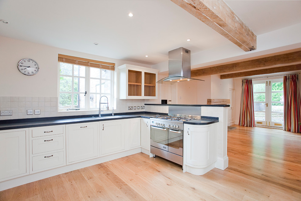 This is an example of a large country open plan kitchen in Other with a double-bowl sink, raised-panel cabinets, white cabinets, granite benchtops, metallic splashback, stainless steel appliances, light hardwood floors and black benchtop.