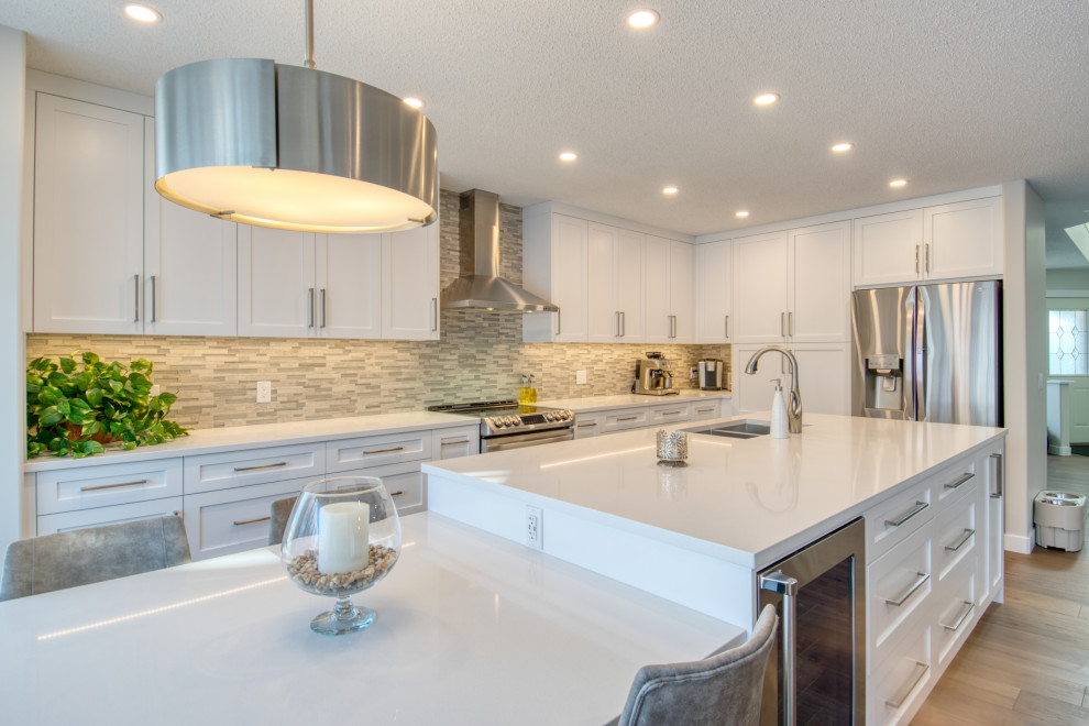 Inspiration for a large transitional u-shaped light wood floor and beige floor kitchen remodel in Calgary with an undermount sink, recessed-panel cabinets, white cabinets, quartz countertops, gray backsplash, matchstick tile backsplash, stainless steel appliances, an island and white countertops
