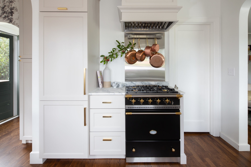 Design ideas for a small traditional galley open plan kitchen in Seattle with an undermount sink, shaker cabinets, beige cabinets, marble benchtops, white splashback, marble splashback, black appliances, medium hardwood floors, a peninsula, brown floor and white benchtop.