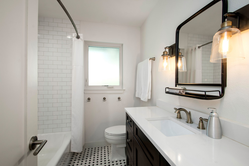 This is an example of a mid-sized kids bathroom in Dallas with flat-panel cabinets, brown cabinets, a drop-in tub, a shower/bathtub combo, a one-piece toilet, white tile, ceramic tile, white walls, porcelain floors, an undermount sink, engineered quartz benchtops, multi-coloured floor, a shower curtain and white benchtops.