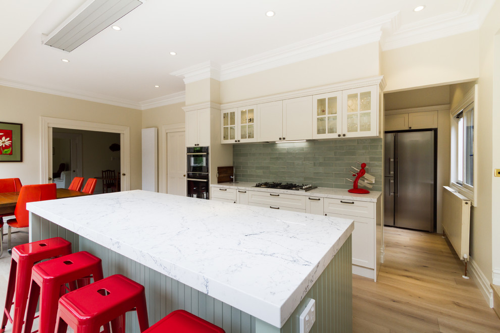 This is an example of a mid-sized traditional galley eat-in kitchen in Melbourne with an undermount sink, shaker cabinets, white cabinets, quartz benchtops, green splashback, subway tile splashback, black appliances, light hardwood floors, with island, beige floor and white benchtop.