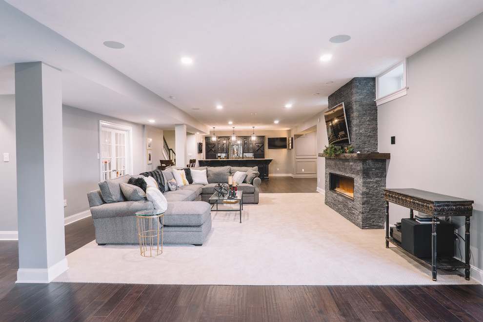 This is an example of a large transitional open concept family room in Philadelphia with grey walls, dark hardwood floors, a standard fireplace, a stone fireplace surround and a wall-mounted tv.