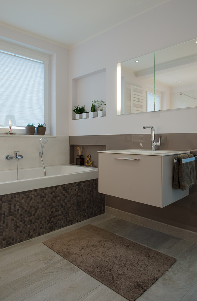 Mid-sized contemporary master bathroom in Dortmund with a drop-in tub, a wall-mount toilet, flat-panel cabinets, beige cabinets, beige tile, glass sheet wall, white walls, painted wood floors, a trough sink and solid surface benchtops.