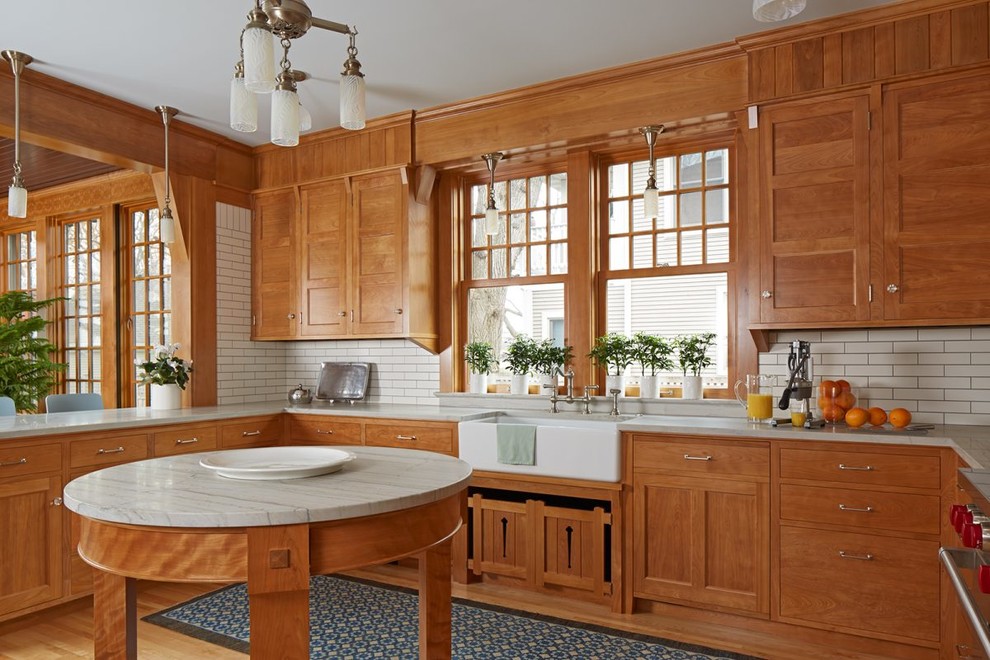 Inspiration for an arts and crafts u-shaped kitchen in Minneapolis with a farmhouse sink, shaker cabinets, medium wood cabinets, white splashback, medium hardwood floors, with island, brown floor and grey benchtop.