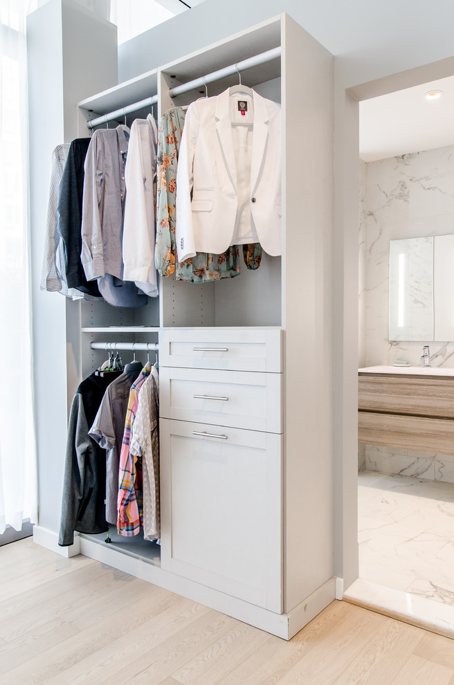 Small modern gender-neutral built-in wardrobe in New York with white cabinets and medium hardwood floors.