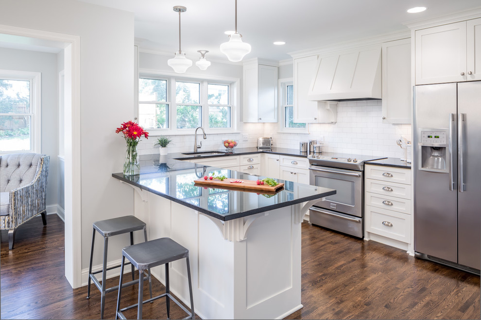 This is an example of a traditional u-shaped kitchen in Minneapolis with an undermount sink, shaker cabinets, white cabinets, white splashback, subway tile splashback, stainless steel appliances, dark hardwood floors and a peninsula.