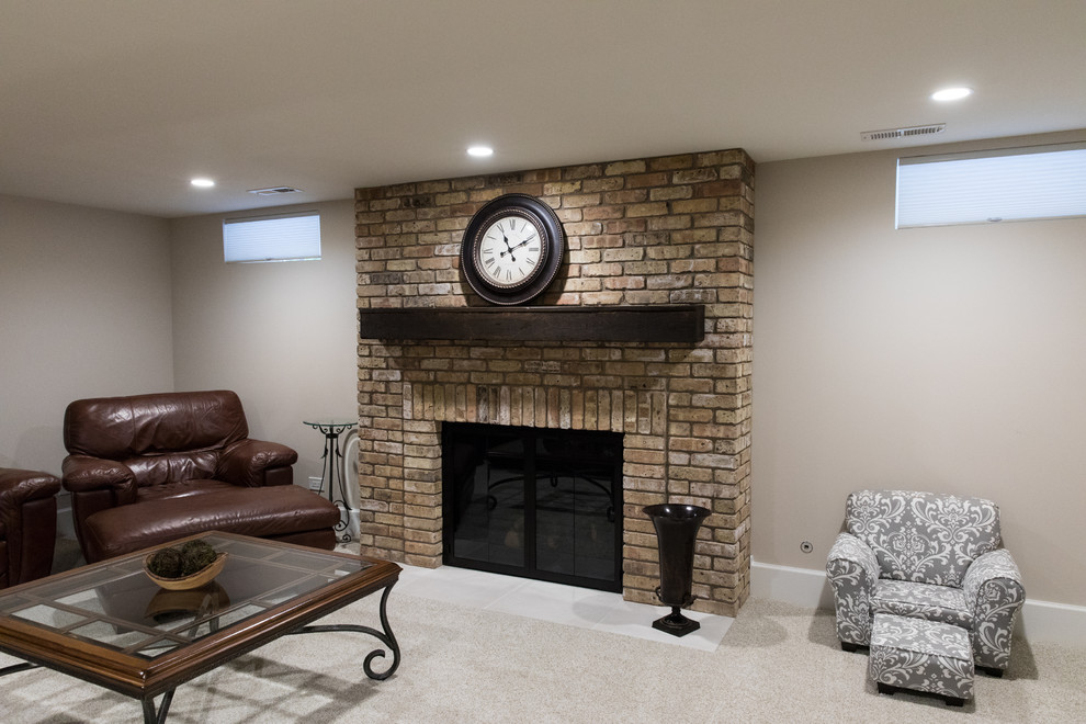 This is an example of a mid-sized traditional fully buried basement in Chicago with beige walls, carpet, a standard fireplace, a brick fireplace surround and beige floor.