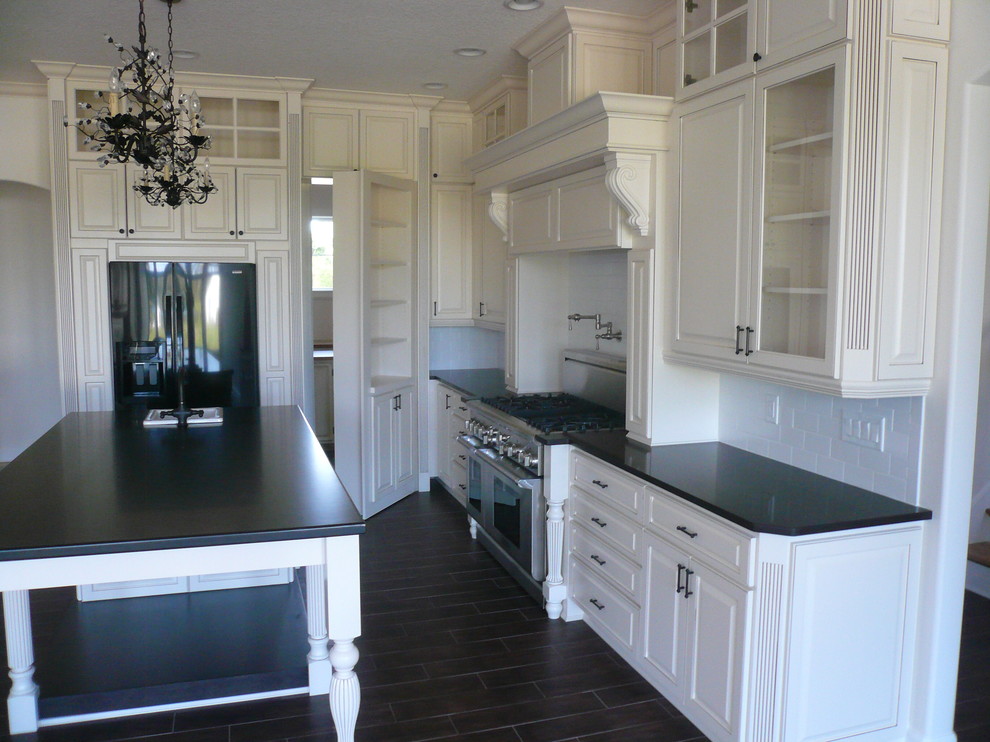 Large traditional galley separate kitchen in Orlando with a farmhouse sink, white cabinets, white splashback, ceramic splashback, black appliances, with island and raised-panel cabinets.