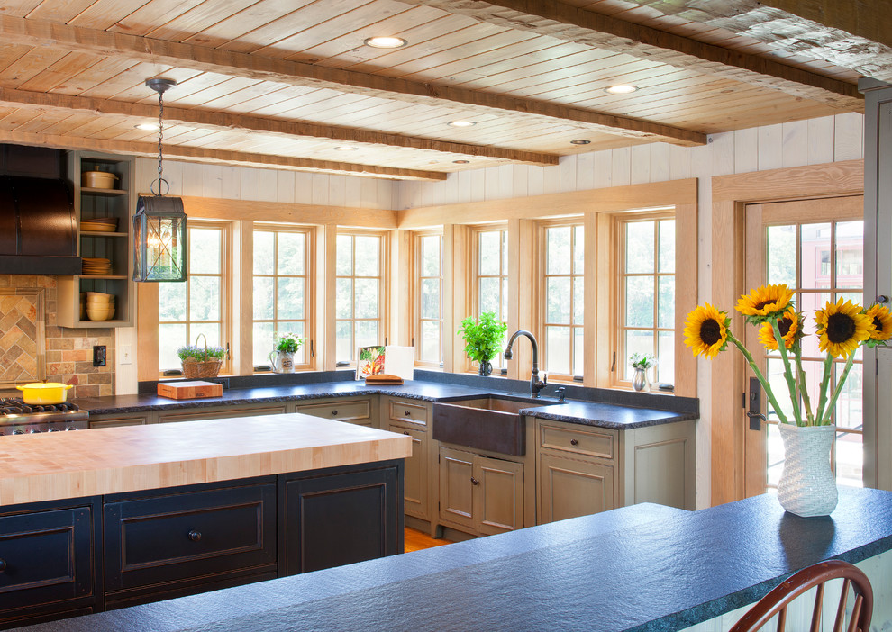 This is an example of a country u-shaped eat-in kitchen in DC Metro with a farmhouse sink, flat-panel cabinets, black cabinets, wood benchtops, black splashback, stone slab splashback and stainless steel appliances.
