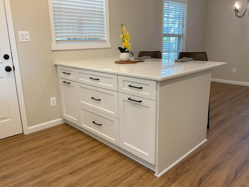 This is an example of a small transitional l-shaped eat-in kitchen in Detroit with an undermount sink, shaker cabinets, white cabinets, quartz benchtops, white splashback, ceramic splashback, stainless steel appliances, medium hardwood floors, with island, brown floor and white benchtop.