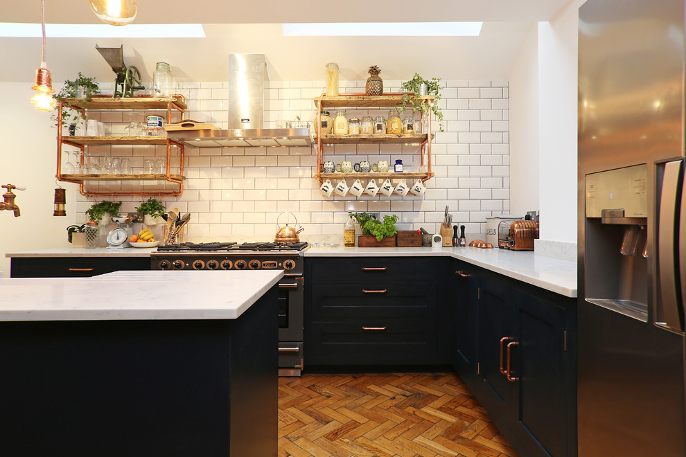 This is an example of an industrial l-shaped kitchen in London with shaker cabinets, black cabinets and with island.