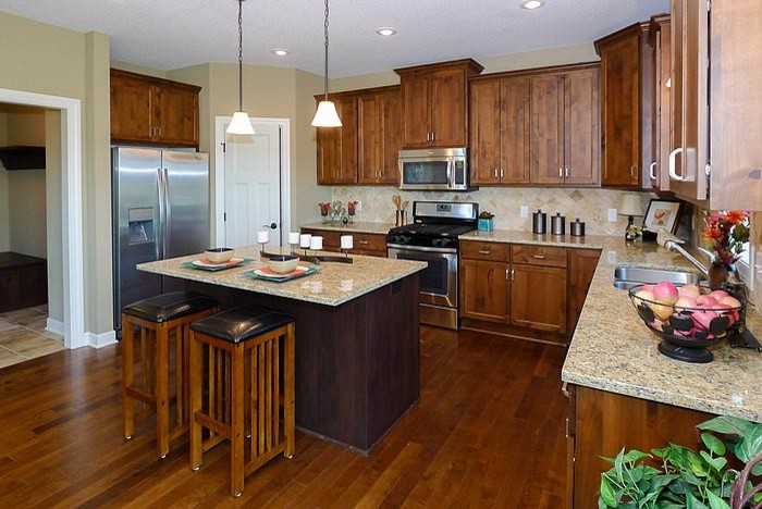Photo of a traditional l-shaped eat-in kitchen in Minneapolis with an undermount sink, flat-panel cabinets, medium wood cabinets, granite benchtops, beige splashback, stone tile splashback and stainless steel appliances.