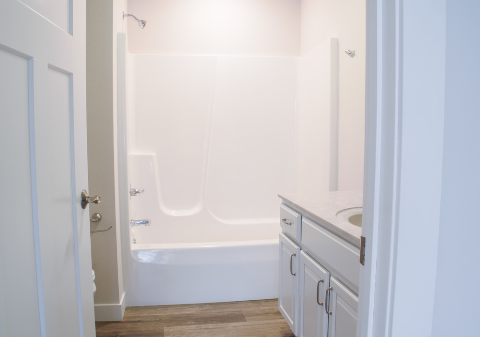 Inspiration for a mid-sized country master bathroom in Other with shaker cabinets, white cabinets, a corner tub, a shower/bathtub combo, a one-piece toilet, white walls, light hardwood floors, an integrated sink, laminate benchtops, brown floor, a shower curtain and multi-coloured benchtops.