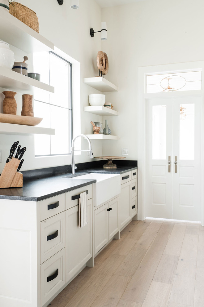 Inspiration for a mid-sized beach style u-shaped open plan kitchen in Salt Lake City with a farmhouse sink, shaker cabinets, white cabinets, stainless steel appliances, light hardwood floors, with island and beige floor.
