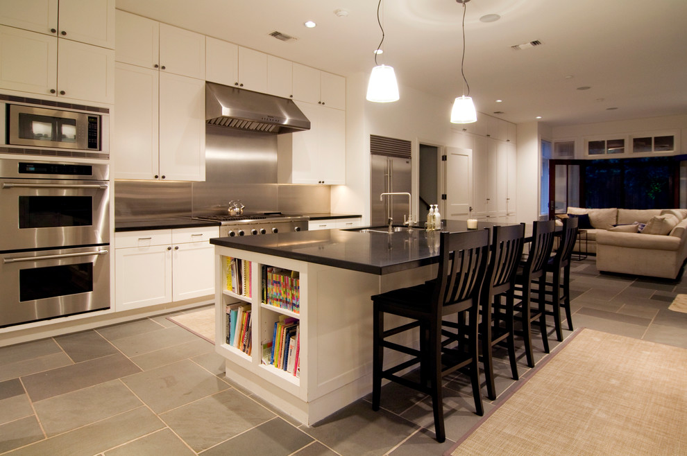 Large modern galley eat-in kitchen in Houston with a double-bowl sink, recessed-panel cabinets, white cabinets, metallic splashback, metal splashback, stainless steel appliances, with island, soapstone benchtops, slate floors and grey floor.