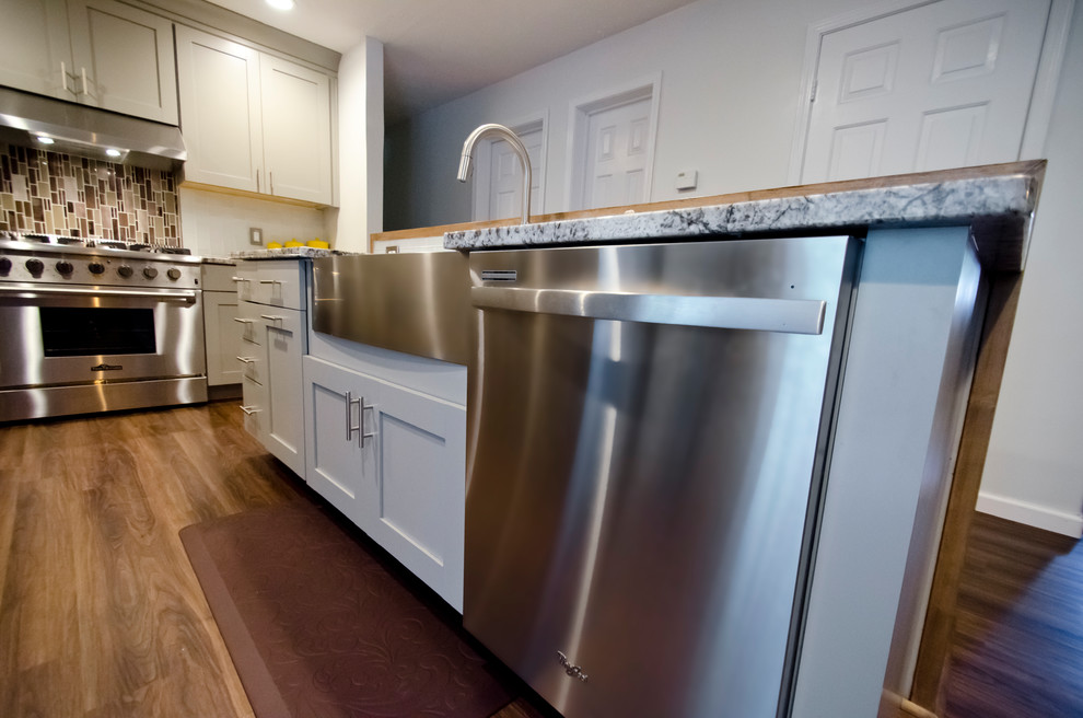 Inspiration for a mid-sized contemporary l-shaped vinyl floor and brown floor eat-in kitchen remodel in Chicago with a farmhouse sink, shaker cabinets, gray cabinets, granite countertops, white backsplash, glass tile backsplash, stainless steel appliances and an island
