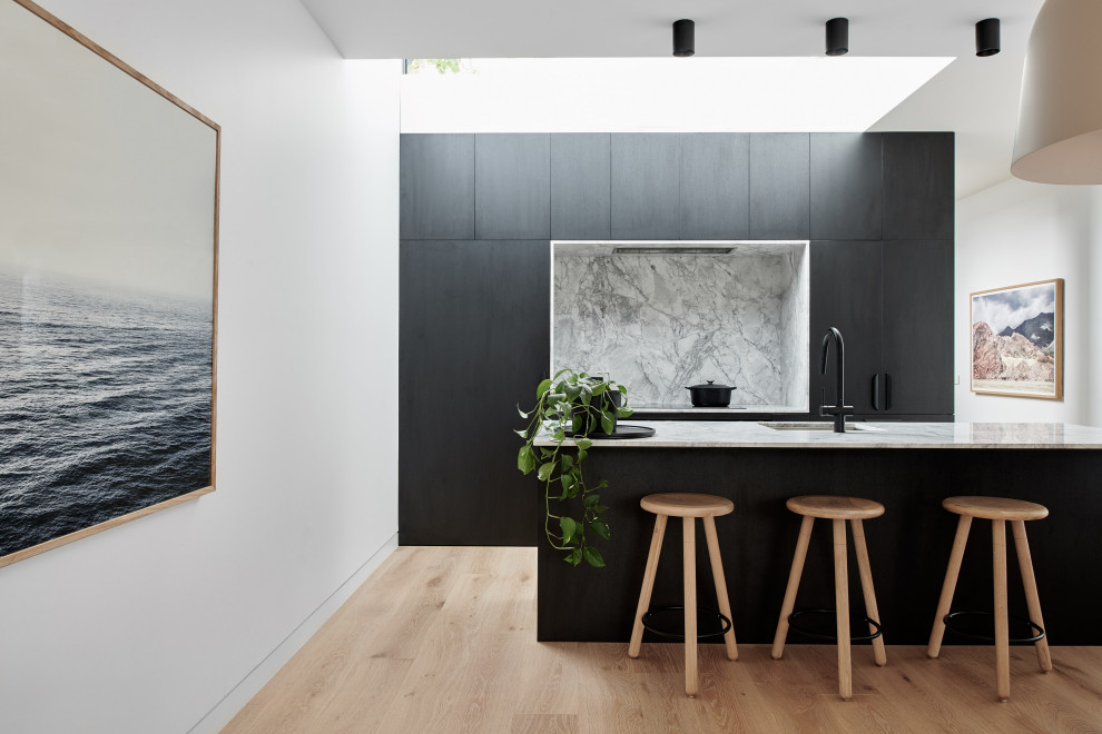 Mid-sized contemporary galley kitchen in Sydney with an integrated sink, flat-panel cabinets, black cabinets, grey splashback, panelled appliances, light hardwood floors, a peninsula, beige floor and grey benchtop.