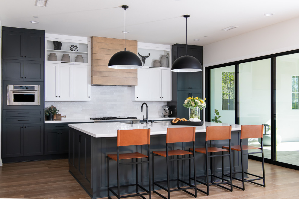 Transitional kitchen photo in Orange County with a farmhouse sink, shaker cabinets, white cabinets, quartzite countertops, white backsplash, subway tile backsplash, stainless steel appliances, an island and white countertops