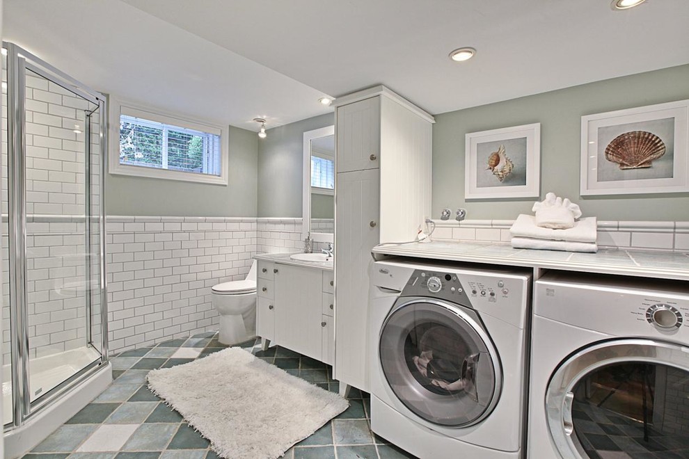 This is an example of a mid-sized l-shaped utility room in Montreal with a drop-in sink, flat-panel cabinets, white cabinets, tile benchtops, terra-cotta floors, a side-by-side washer and dryer and grey walls.