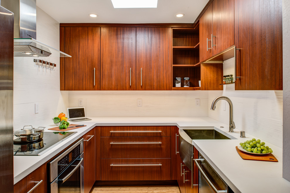 This is an example of a small contemporary u-shaped eat-in kitchen in San Francisco with a farmhouse sink, flat-panel cabinets, dark wood cabinets, solid surface benchtops, white splashback, porcelain splashback, stainless steel appliances, bamboo floors and no island.