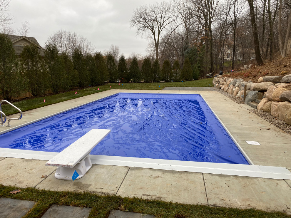 Diseño de piscina costera grande en patio trasero con adoquines de hormigón