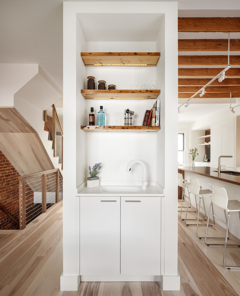 Design ideas for a small modern single-wall wet bar in Boston with an integrated sink, flat-panel cabinets, white cabinets, solid surface benchtops, white splashback and light hardwood floors.