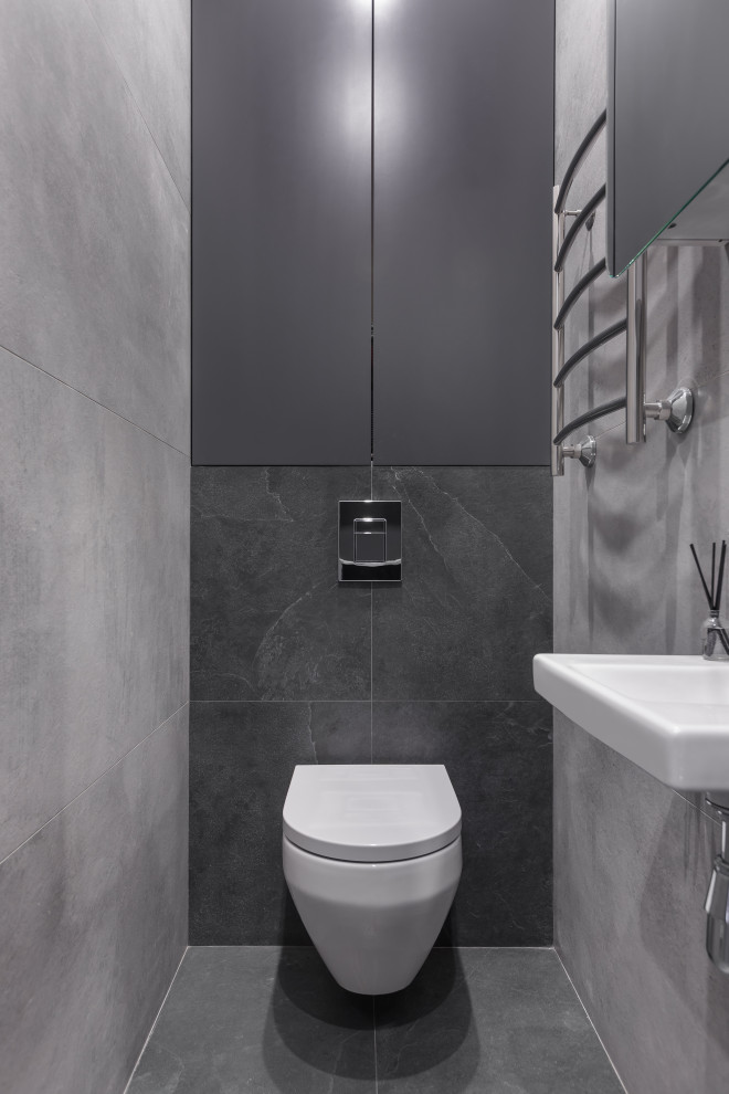 Cette image montre un petit WC suspendu design avec un placard à porte plane, des portes de placard noires, un carrelage gris, des carreaux de porcelaine, un mur gris, un sol en carrelage de porcelaine, un plan vasque et un sol noir.