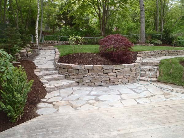 This is an example of a large traditional backyard shaded garden in Other with a retaining wall and natural stone pavers.
