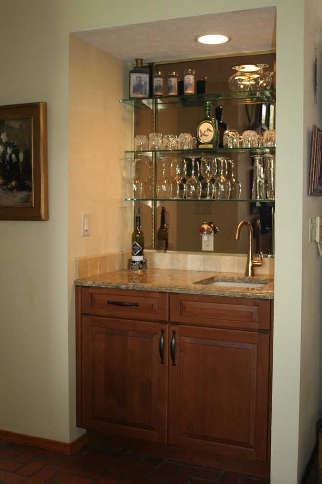 This is an example of a mid-sized traditional l-shaped wet bar in Albuquerque with an undermount sink, raised-panel cabinets, medium wood cabinets, solid surface benchtops, beige splashback, stone tile splashback, brick floors and red floor.