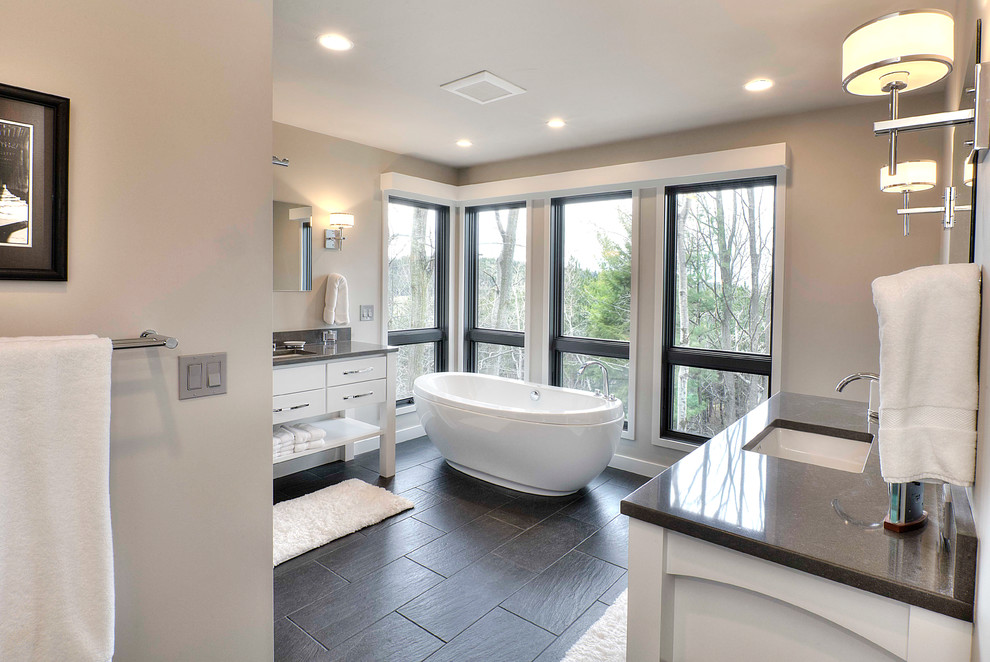 Inspiration for a mid-sized transitional master bathroom in Other with an undermount sink, furniture-like cabinets, white cabinets, engineered quartz benchtops, a freestanding tub, an alcove shower, a one-piece toilet, gray tile, ceramic tile, grey walls and ceramic floors.