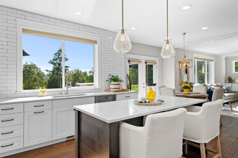 Example of a mid-sized beach style l-shaped light wood floor and brown floor eat-in kitchen design in Seattle with an undermount sink, shaker cabinets, white cabinets, quartzite countertops, white backsplash, subway tile backsplash, stainless steel appliances, an island and white countertops