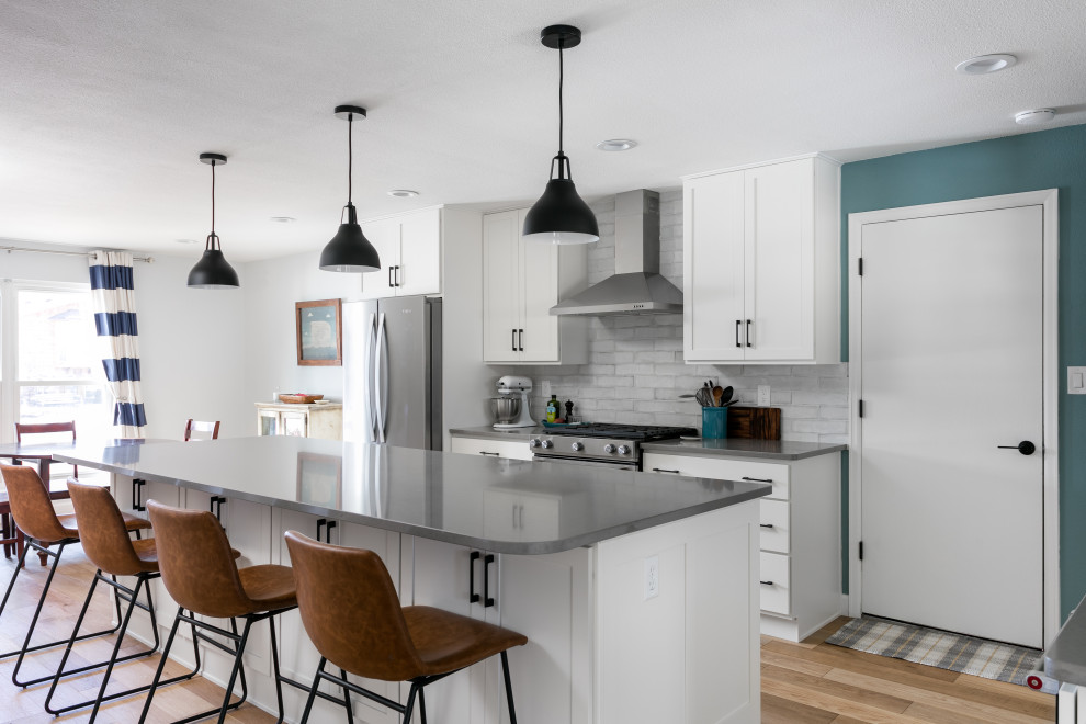 Inspiration for a mid-sized transitional l-shaped light wood floor and brown floor eat-in kitchen remodel in Denver with an undermount sink, shaker cabinets, white cabinets, quartz countertops, white backsplash, porcelain backsplash, stainless steel appliances, an island and gray countertops