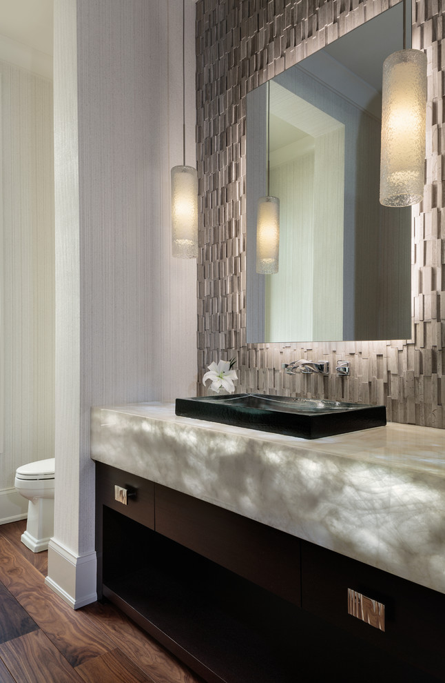 Photo of a mid-sized contemporary powder room in Miami with flat-panel cabinets, brown cabinets, ceramic floors, onyx benchtops, brown floor, gray tile, grey walls, a vessel sink and grey benchtops.