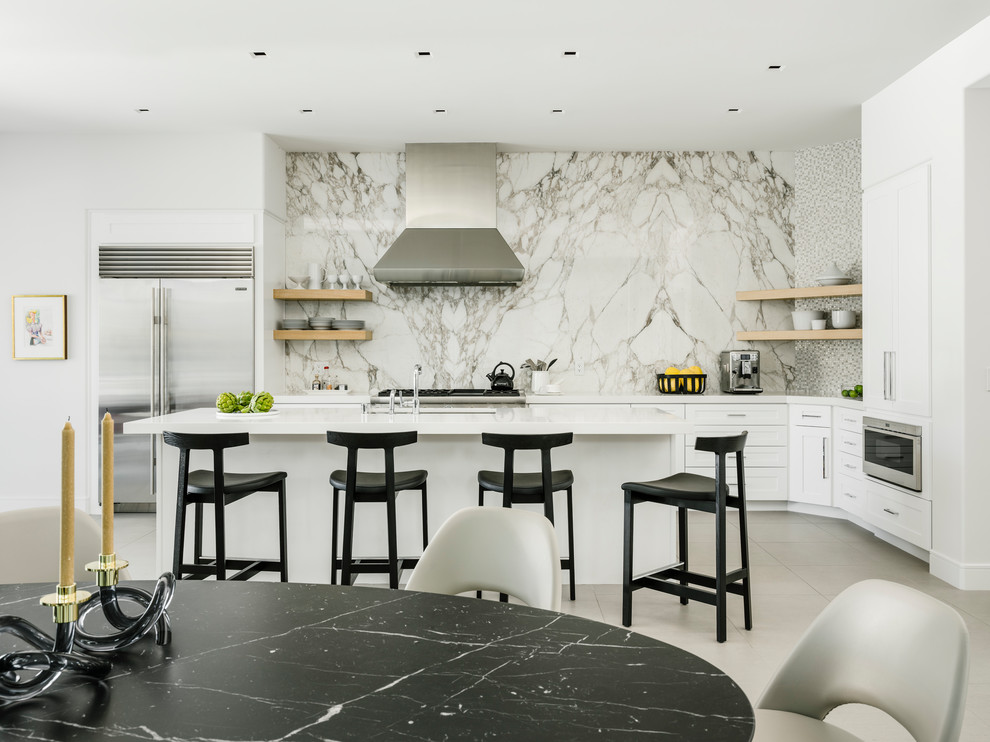 Mid-sized contemporary galley open plan kitchen in Los Angeles with shaker cabinets, white cabinets, quartz benchtops, white splashback, marble splashback, stainless steel appliances, porcelain floors, with island, grey floor, white benchtop and an undermount sink.