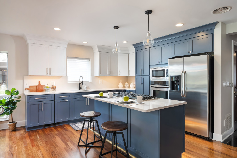 Kitchen - transitional l-shaped medium tone wood floor and brown floor kitchen idea in New York with an undermount sink, shaker cabinets, blue cabinets, white backsplash, stone slab backsplash, stainless steel appliances, an island and white countertops