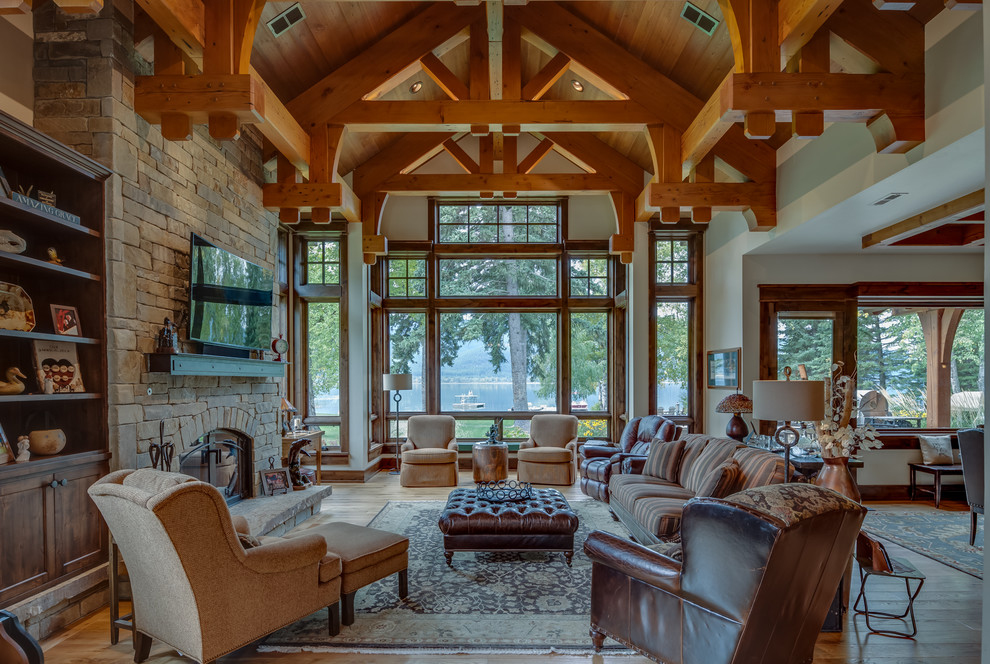 Photo of a large country formal enclosed living room in Other with beige walls, light hardwood floors, a standard fireplace, a stone fireplace surround, a wall-mounted tv and brown floor.