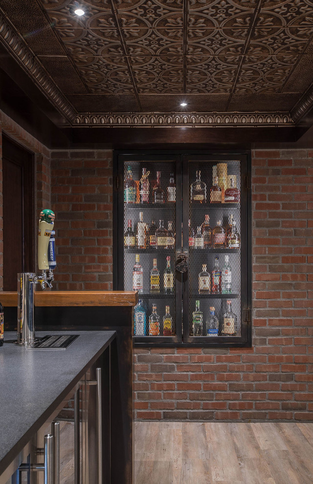 This is an example of a large industrial galley seated home bar in Detroit with vinyl floors, beige floor, black cabinets, wood benchtops, red splashback, brick splashback, brown benchtop and an undermount sink.