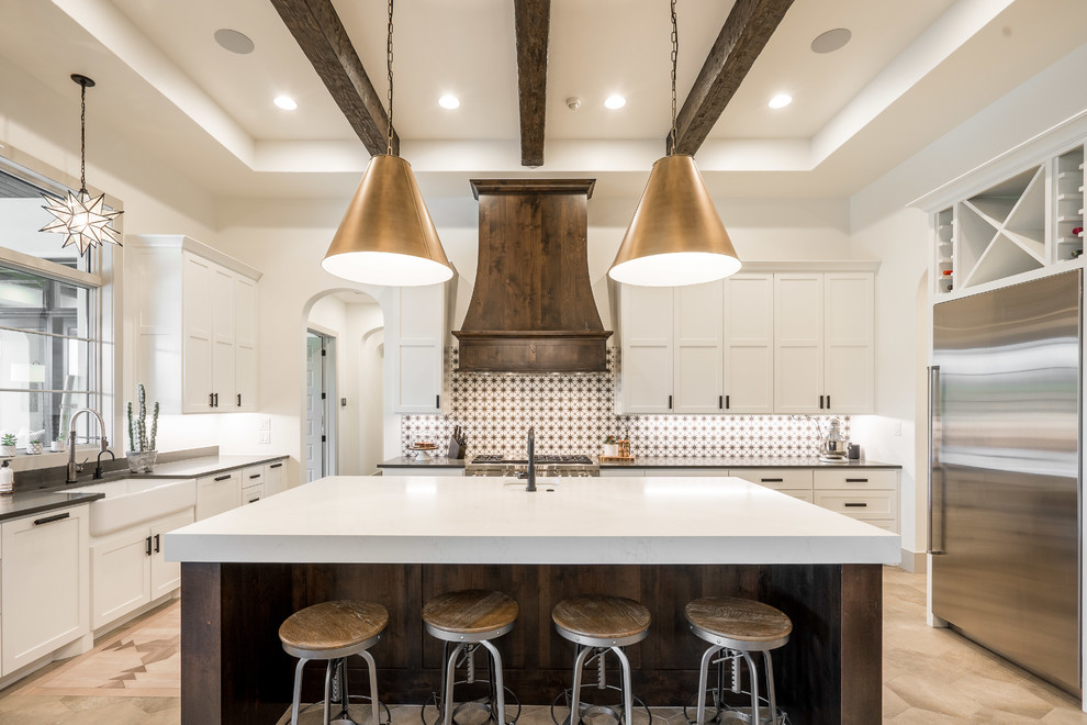 Mediterranean u-shaped kitchen in Austin with a farmhouse sink, shaker cabinets, white cabinets, multi-coloured splashback, stainless steel appliances, with island, beige floor and black benchtop.