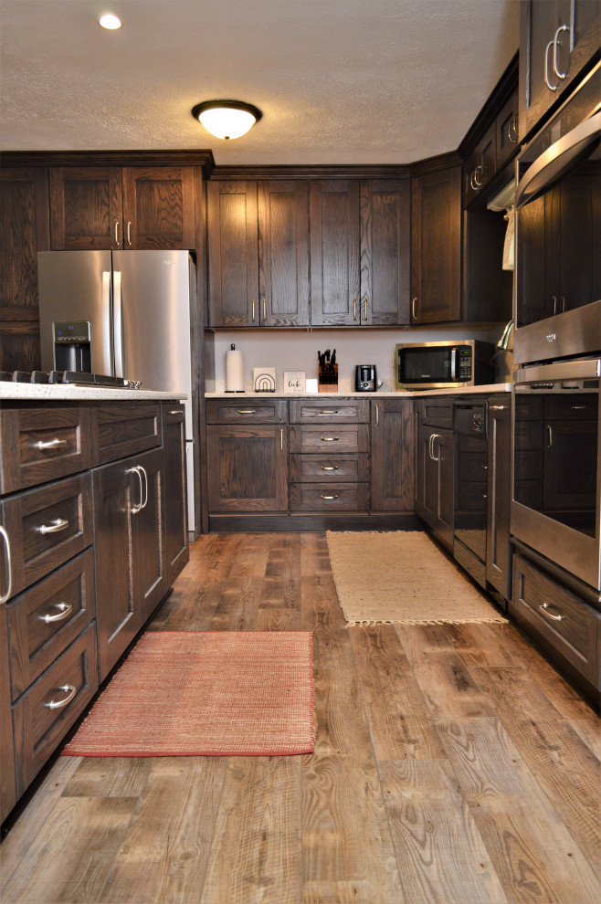 This is an example of a mid-sized country l-shaped open plan kitchen in Chicago with an undermount sink, shaker cabinets, dark wood cabinets, quartzite benchtops, stainless steel appliances, laminate floors, with island, brown floor and grey benchtop.
