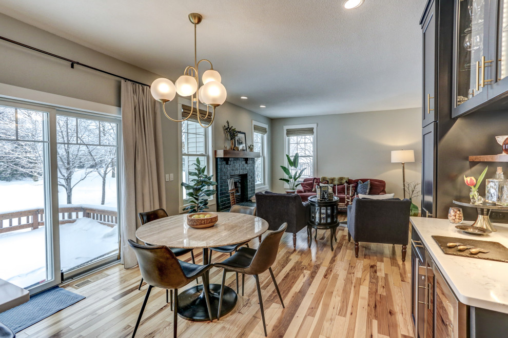 Mid-sized transitional open concept living room in Minneapolis with grey walls, light hardwood floors, a standard fireplace, a brick fireplace surround and brown floor.